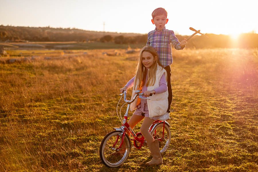 Niño levantando un palo mientras juega en bici al atardecer